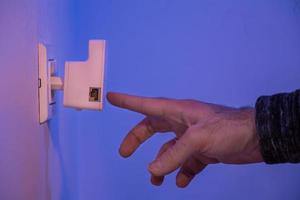 El hombre presione con el dedo el botón WPS en el repetidor wifi que se encuentra en la toma de corriente de la pared foto