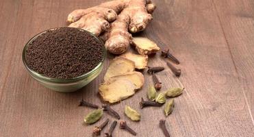 Black Tea Powder or dry dust tea powder, chai patti isolated in wooden bowl with Cardamom, Clove and Ginger. photo