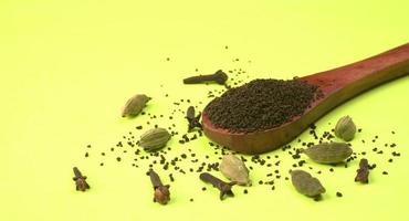 polvo de té negro o polvo de té en polvo seco, chai patti aislado en un tazón de madera con cardamomo, clavo y jengibre. foto
