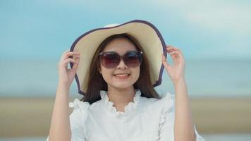 Close-up of an Asian girl wearing hat and glasses by the sea