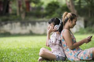 Mother and daughter reading a fairytale to her daughter listen sound with headphone in the park photo