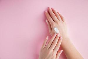 A young woman is applying cream to her hands. Spa and body care concept on a pink background. Image for advertising. photo