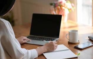 A young woman is using a laptop and writing a report. She works from home. photo