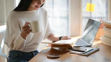 una foto de un joven estudiante sosteniendo una taza de café y leyendo en un hermoso café ligero.