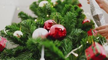 aziatische vrouw met kleine rode ballen versieren de kerstboom viert het nieuwe jaar in de woonkamer thuis. video