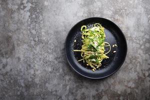 Spaghetti with spinach, pine nuts and parmesan cheese in a black plate on a gray table photo