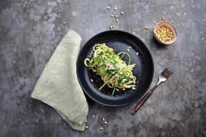 Spaghetti with spinach, pine nuts and parmesan in a plate on a gray table and a fork photo