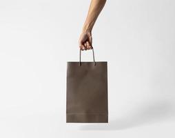 Hand holding blank brown paper bag for mockup template advertising and branding on gray background. photo