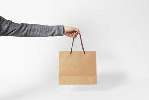 Hand holding blank brown paper bag for mockup template advertising and branding on gray background. photo