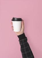 mano sosteniendo una taza de papel de café. maqueta para el diseño creativo de la marca sin fondo rosa. foto