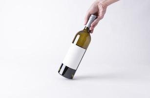 mano sosteniendo una botella de vino para maqueta. etiqueta en blanco sobre un fondo gris. foto