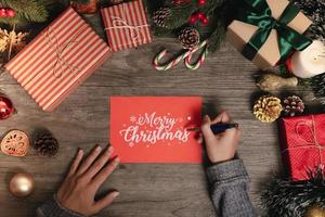 Tarjeta de felicitación de escritura a mano texto feliz navidad con decoración navideña en la mesa de madera. foto