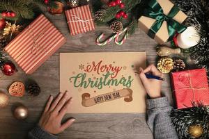 Tarjeta de felicitación de escritura a mano texto feliz navidad con decoración navideña en la mesa de madera. foto