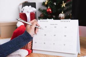 Empresaria escribiendo planificador de calendario en vacaciones de Navidad en la oficina con decoración navideña en la mesa. foto