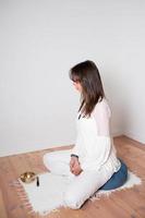 Adult caucasian woman seen portrait from her left side. Sitting cross legged yoga pose. Blue yoga cushion and cupper singing bowl. photo