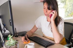 Caucasian adult woman working at home. Taking notes and using her contact phone photo