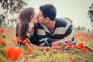 Young couple kissing while lying on the grass in a field of red poppies