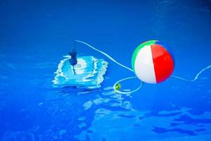 Colorful beach ball floating in pool and next to him underwater a cleaning robot photo