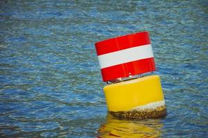 Yellow red and white steel navigational floating buoy in the blue sea water