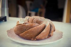 Banana cake with chocolate chips and powdered sugar over it is placed on a ceramic pink plate.