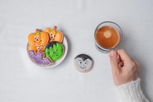 woman hand holding coffee cup during eating funny Halloween Cookies. Happy Halloween day, Trick or Threat, Hello October, fall autumn, Traditional, party and holiday concept photo