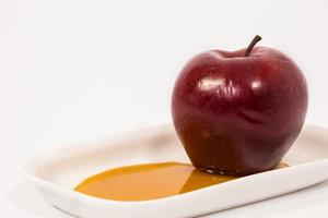 Manzana roja sobre un plato blanco con miel aislado sobre un fondo blanco.