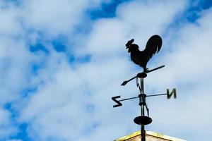 Black weathervane in the form of a rooster. The background has a blue sky with clouds. photo