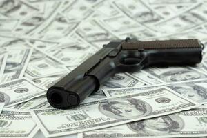 Black gun pistol on stack money 100 dollars background