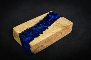 Casting blue epoxy resin with nature burl maple wood cube on black background photo