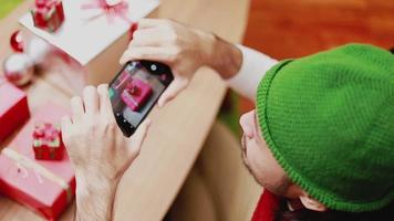 homens asiáticos que pegam uma caixa de foto-presente no smartphone decoram a árvore de Natal que comemora o ano novo na sala de estar. video