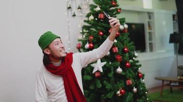 Asian man using a smartphone video chat presents a gift box with friends.