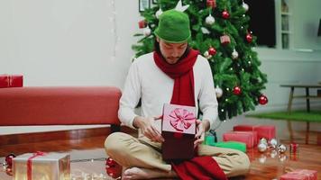 surpresa homens asiáticos abrem a caixa de presente na sala de estar em casa, tendo uma árvore de Natal ao fundo.