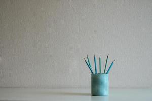 Close up of pastel pencils in the blue glass on the desk at gray wall background photo