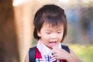 Adorable Asian baby child girl black haired girl braiding on the head. She is sticking out tongue and using her index finger to touch the tip of the tongue. Sweet smile with against melt background. photo