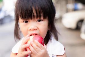 Portrait of child girl eating red apple and looking at camera. Head short of healthy kid eating fresh fruit for snack time. Children aged 3 years old. photo