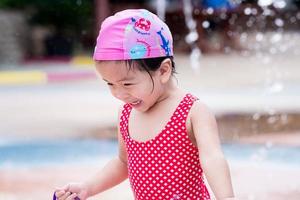 Portrait of happy cute girl playing water. Child wearing red swim suit and pink swim hat. Sweet smile kid it fun. In summer time. photo