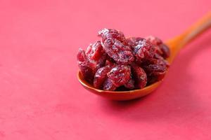dried cranberries on a wooden spoon on red background photo
