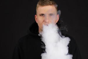 Men smoke an electronic cigarette on the dark background. Selective focus