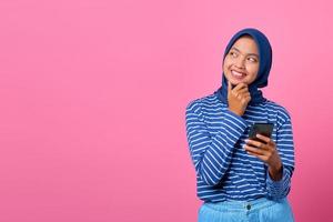 Retrato de joven mujer asiática pensando en la pregunta con la mano en la barbilla mientras sostiene el teléfono inteligente
