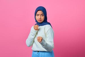 Portrait of angry young Asian woman showing boxer gesture on pink background photo