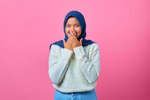 Retrato de mujer asiática joven sonriente que cubre la boca con la mano sobre fondo de color rosa