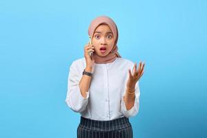 Retrato de mujer asiática joven sorprendida hablando por teléfono móvil con las manos levantadas foto