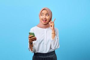Retrato de mujer asiática joven emocionada que sostiene el teléfono móvil y el dedo levantado porque tienen soluciones foto