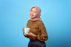 Hermosa joven asiática sosteniendo la taza y bebiendo té sobre fondo azul.
