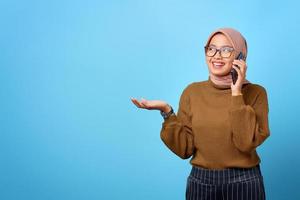 Retrato de feliz bella mujer asiática hablando por teléfono móvil sobre fondo azul.