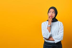 Pensive young Asian woman looks seriously thinking about a question on yellow background photo
