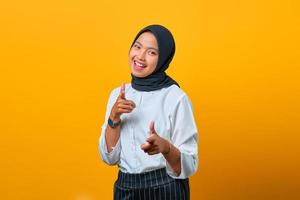 Portrait of smiling young Asian woman pointing fingers at camera on yellow background