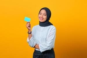 Atractiva joven mujer asiática riendo y sosteniendo una tarjeta de crédito sobre fondo amarillo foto