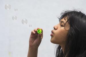 una niña que sostiene una máquina de hacer burbujas y las sopla. foto