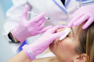 Aesthetic doctor injecting botox into the forehead of her middle-aged patient. photo